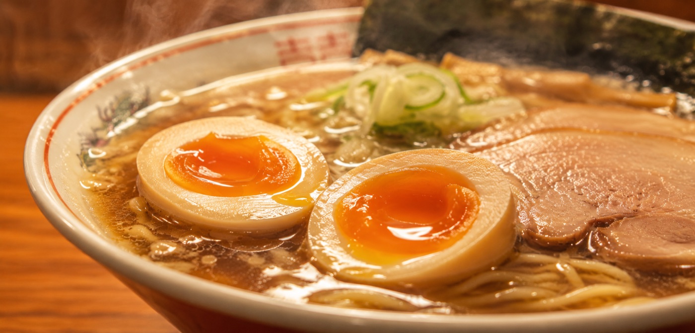 半熟の味玉がのった、湯気の立つラーメンのクローズアップ