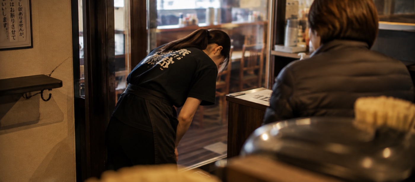 店内で深く頭を下げる、エプロン姿のスタッフの後ろ姿